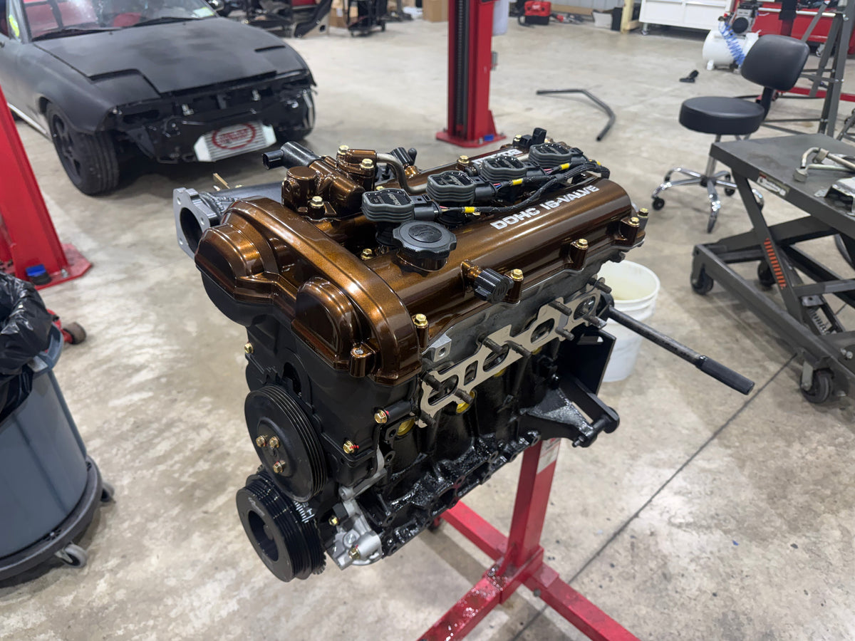 Assembled Miata engine with bronze valve cover and coil packs on a red engine stand in the Napp Motorsports shop