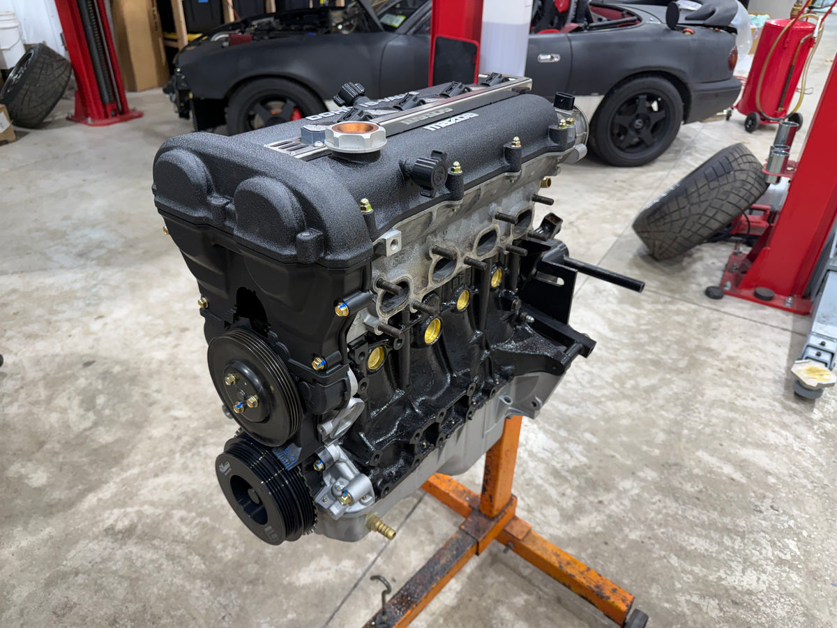 Assembled Miata engine with textured black valve cover on an orange engine stand