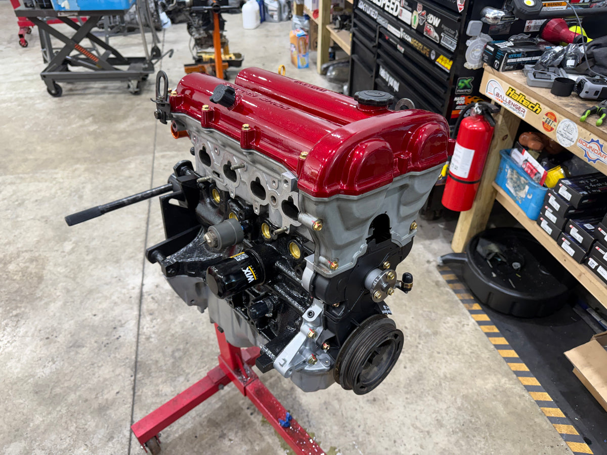 Assembled Miata engine with red valve cover and oil filter on a red engine stand