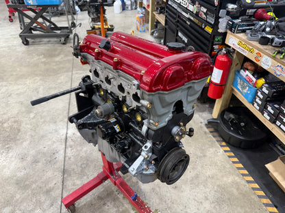 Assembled Miata engine with red valve cover and oil filter on a red engine stand