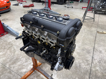 Assembled Miata engine with textured black valve cover and coil packs on an orange engine stand