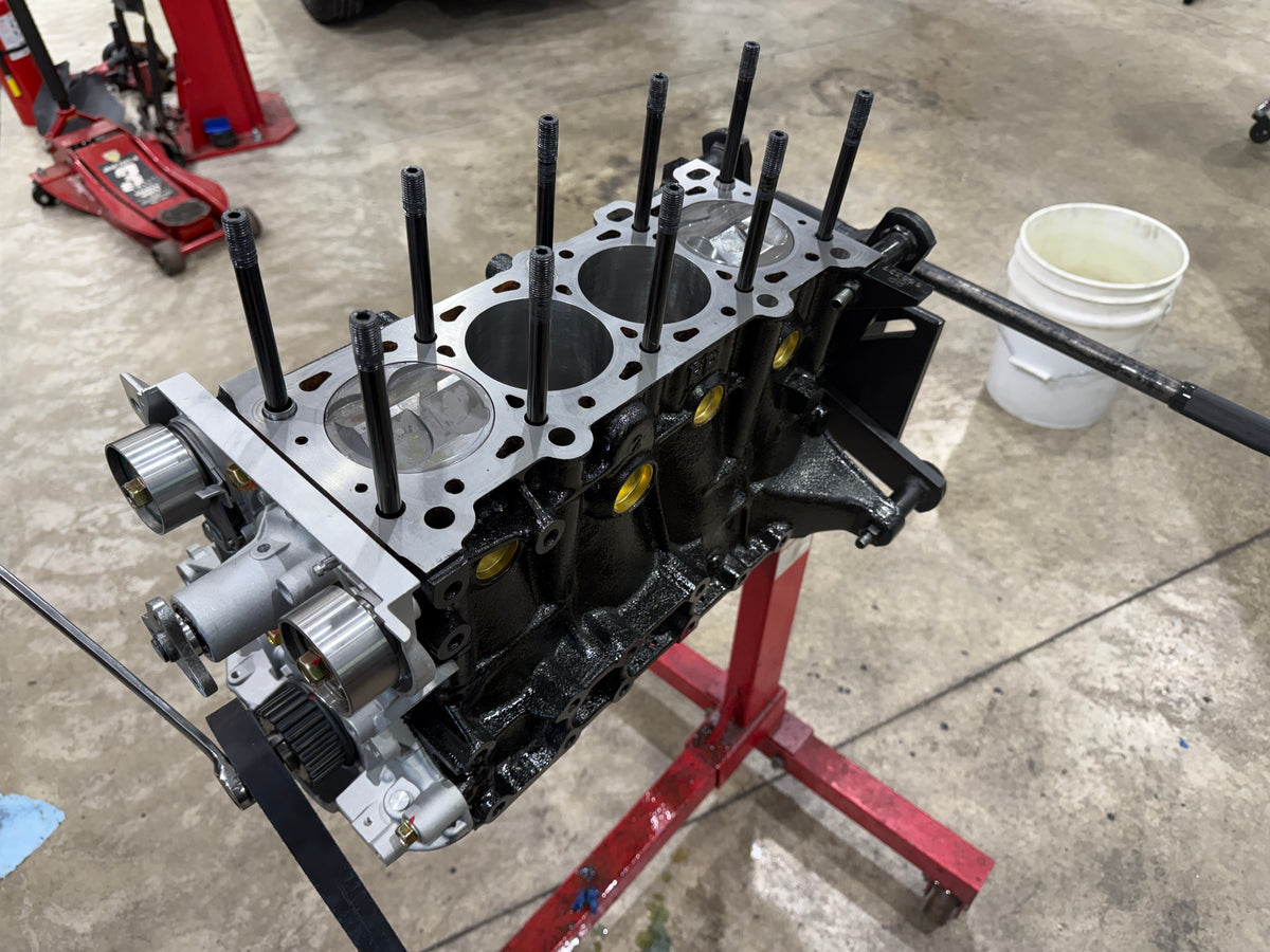 Miata short block on an engine stand with head studs installed and pistons visible in the bores