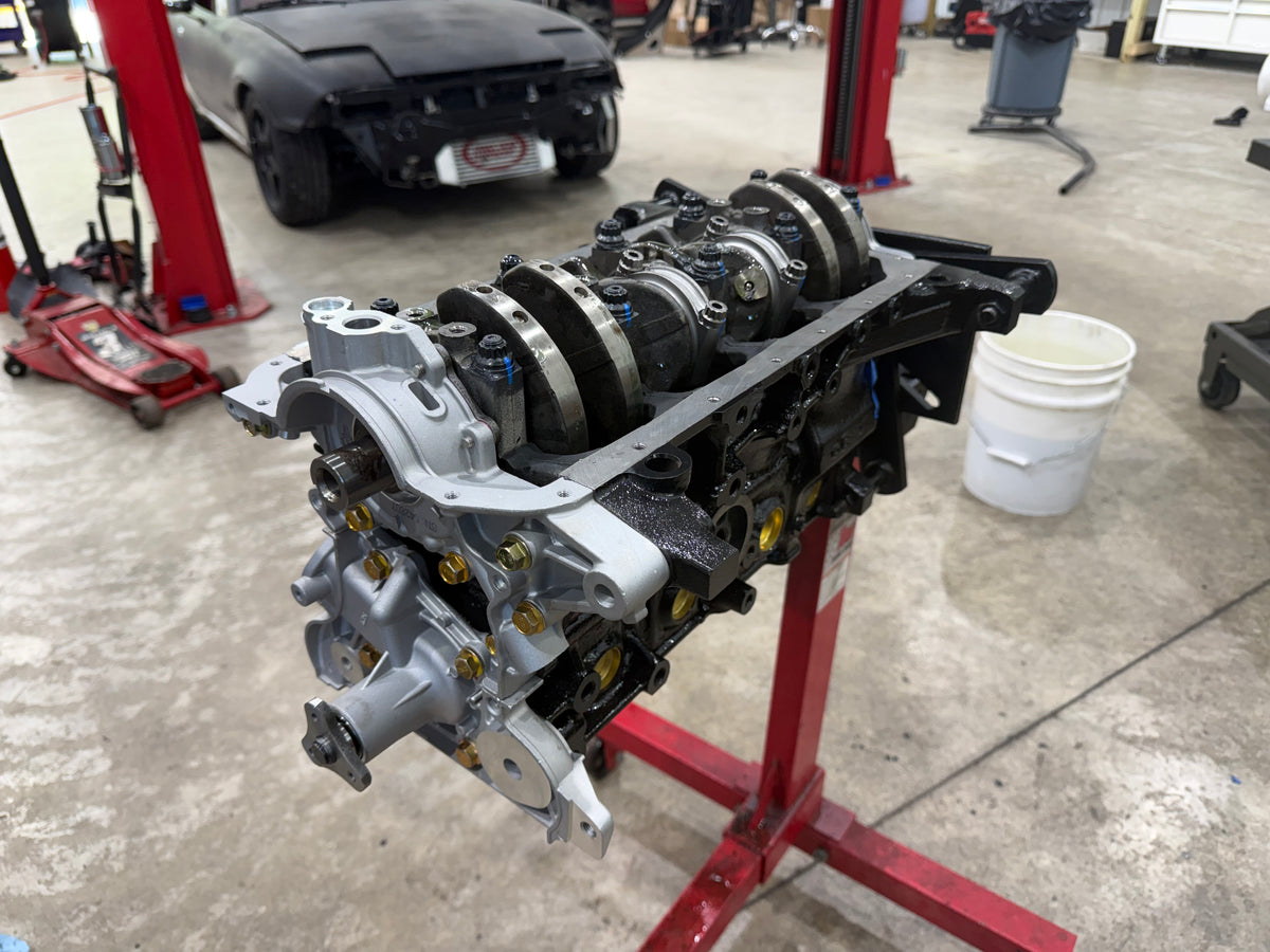 Miata engine block upside down on a stand showing the crankshaft, connecting rods and bearing caps