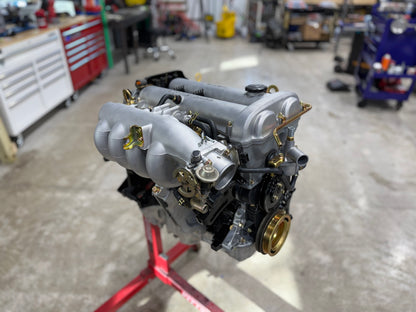 Assembled Miata engine on a build stand with silver intake manifold and throttle body