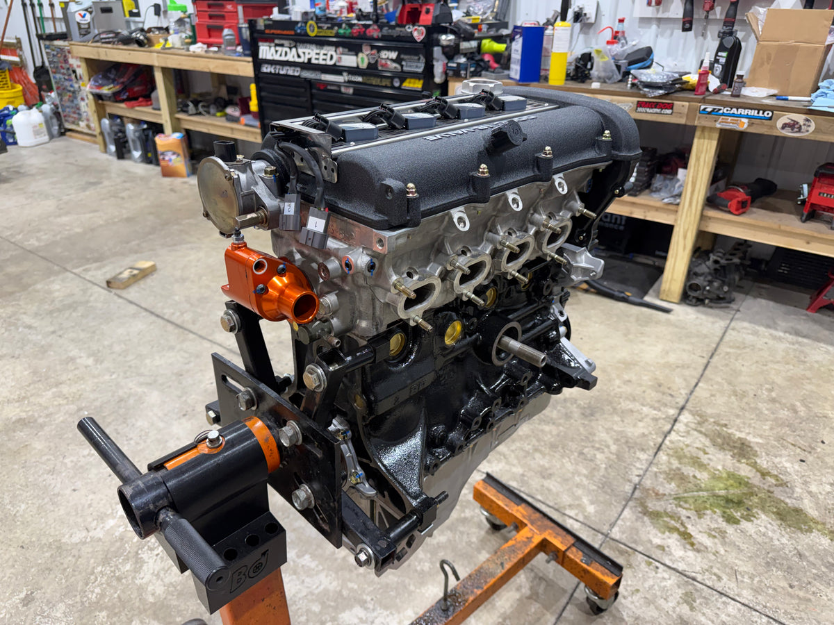 Assembled Miata engine with black valve cover, throttle body and orange coolant outlet on an engine stand