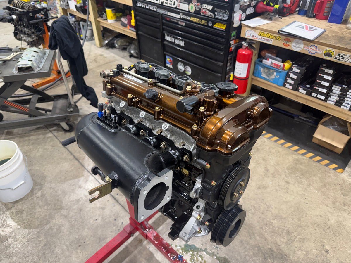 Assembled Miata engine with bronze valve cover and black intake manifold on a red engine stand