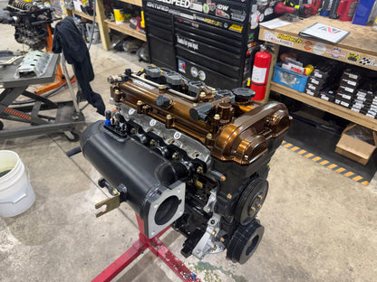 Assembled Miata engine with bronze valve cover and black intake manifold on a red engine stand