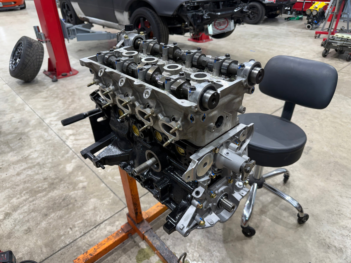 Miata long block on an engine stand with the valve cover off, camshafts and cam caps in view